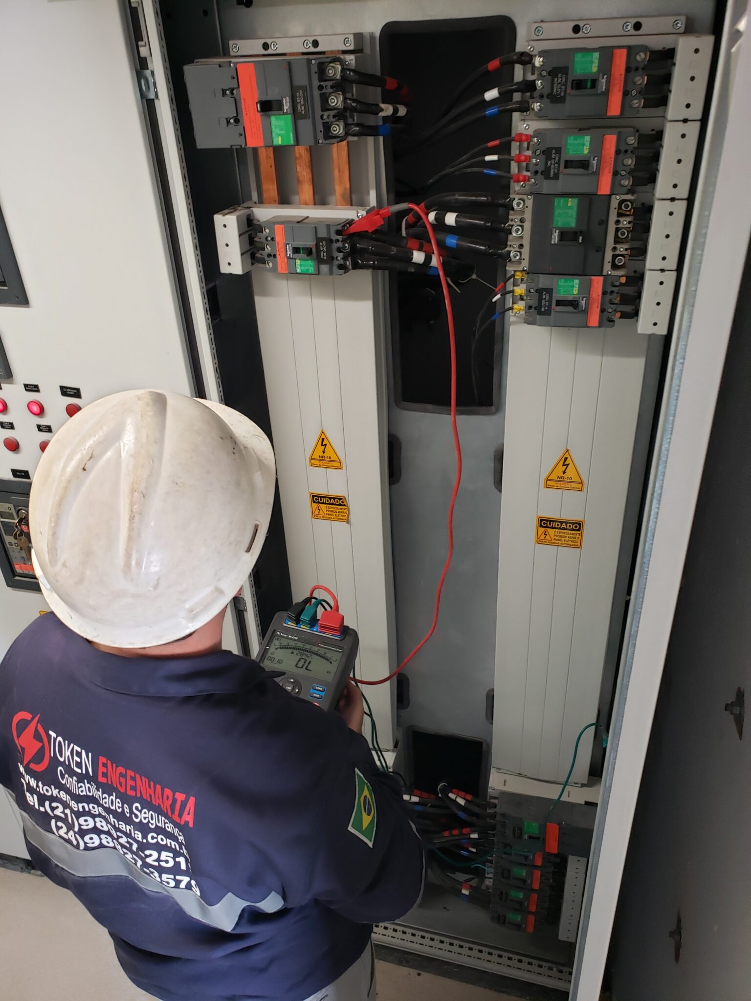 Dois técnicos da Token Engenharia inspecionando painel elétrico industrial aberto com cabeamento — estudo de arco elétrico NR-10