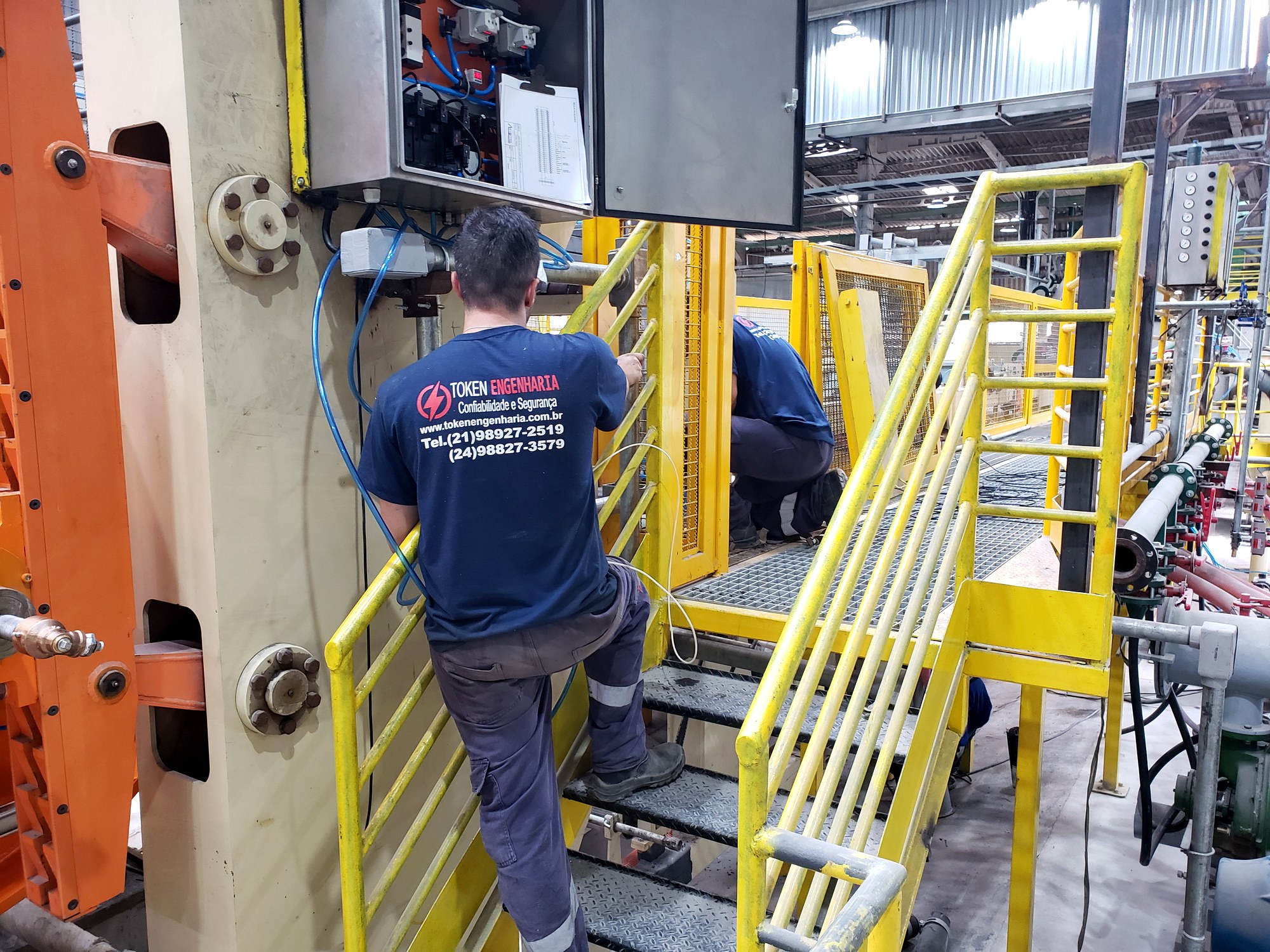 Técnico da Token Engenharia de uniforme inspecionando painel elétrico industrial antes de serviço energizado