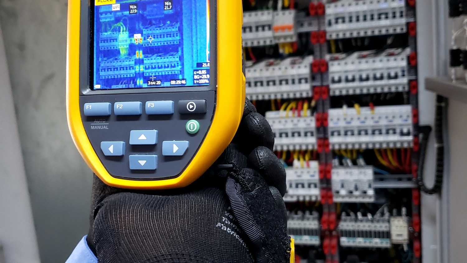 Técnico com câmera termográfica Fluke realizando inspeção termográfica de painel elétrico industrial aberto com disjuntores