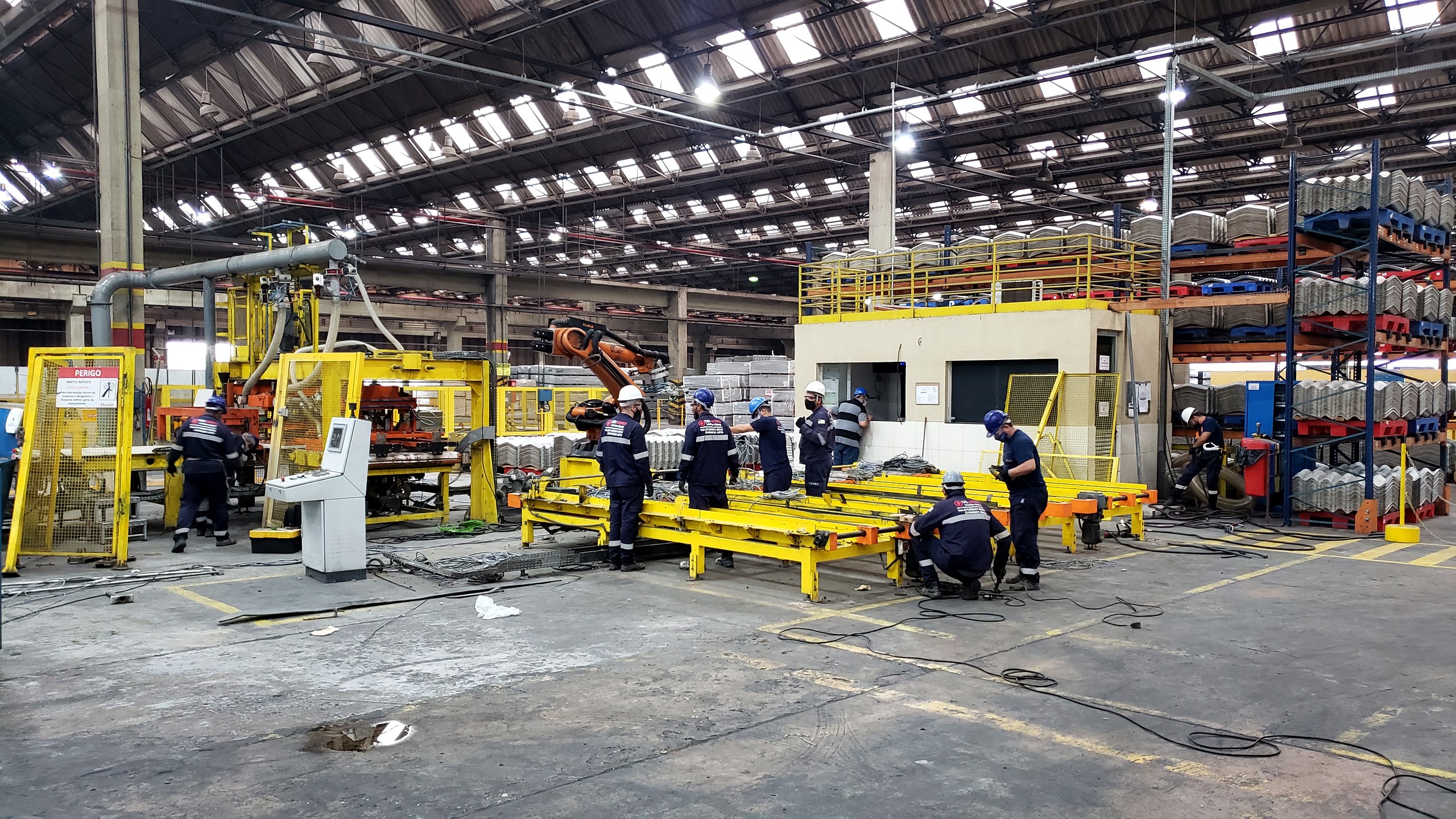 Equipe técnica da Token em planta industrial durante serviço de manutenção elétrica, com linha de produção ao fundo