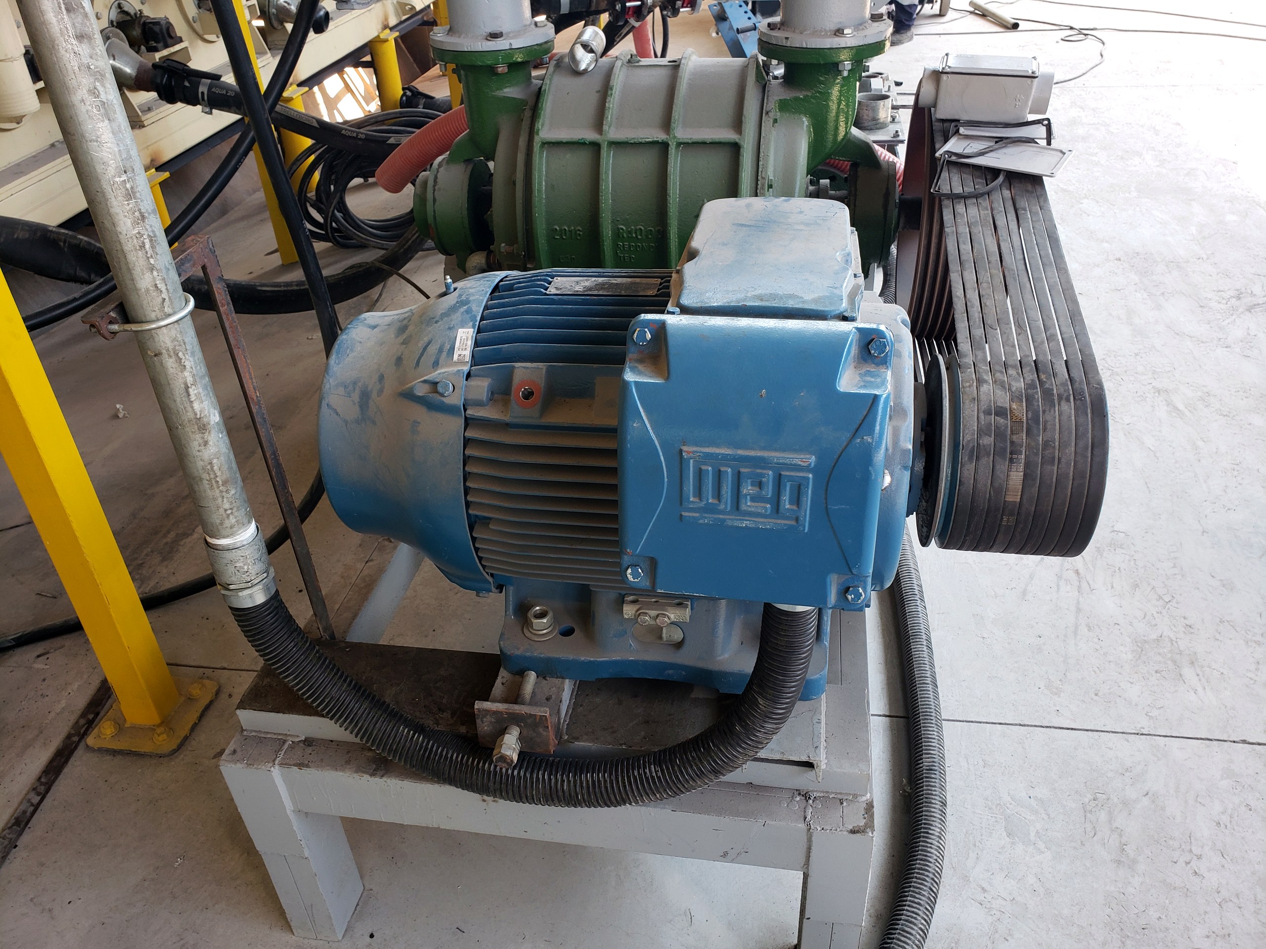 Motor elétrico WEG azul acoplado a soprador industrial por correias, em planta industrial