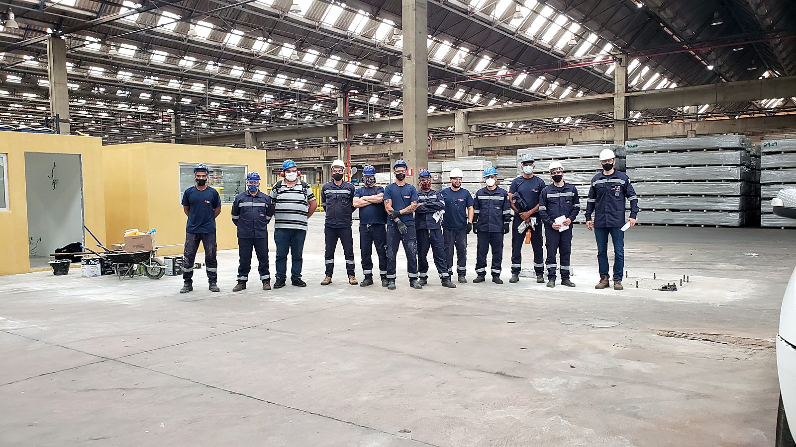 Galpão industrial vazio antes da montagem, com a equipe Token e os pontos de fixação marcados no piso