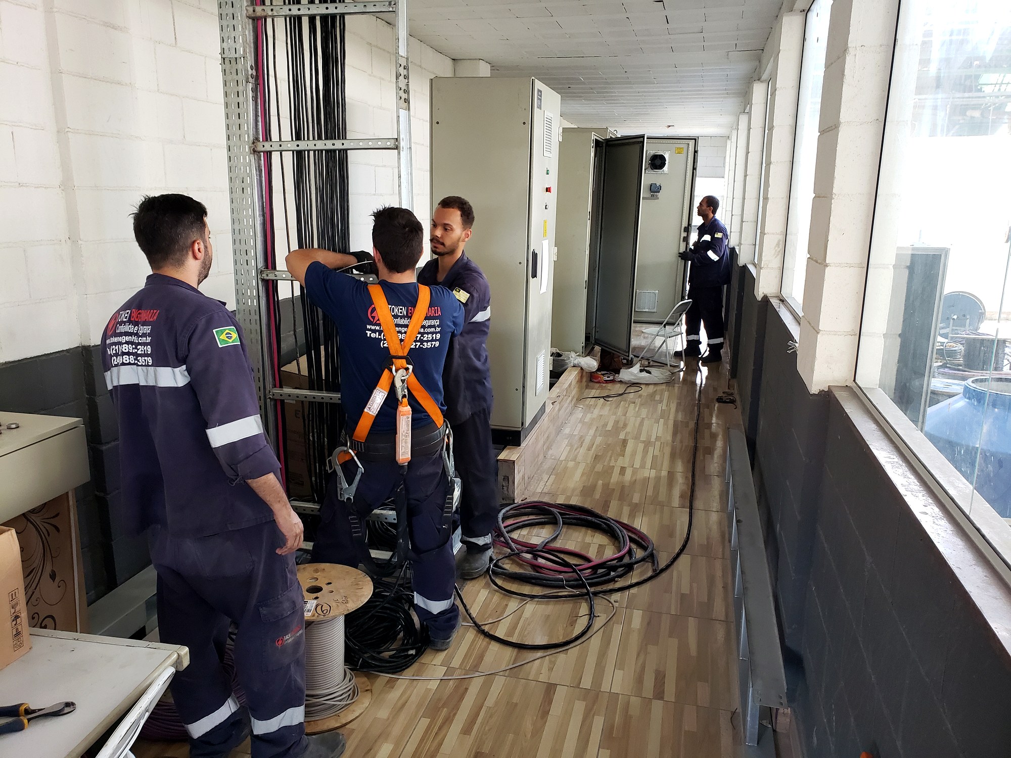 Equipe da Token Engenharia lançando cabos na prumada e eletrocalha junto a quadros elétricos em corredor técnico de prédio durante projeto elétrico predial