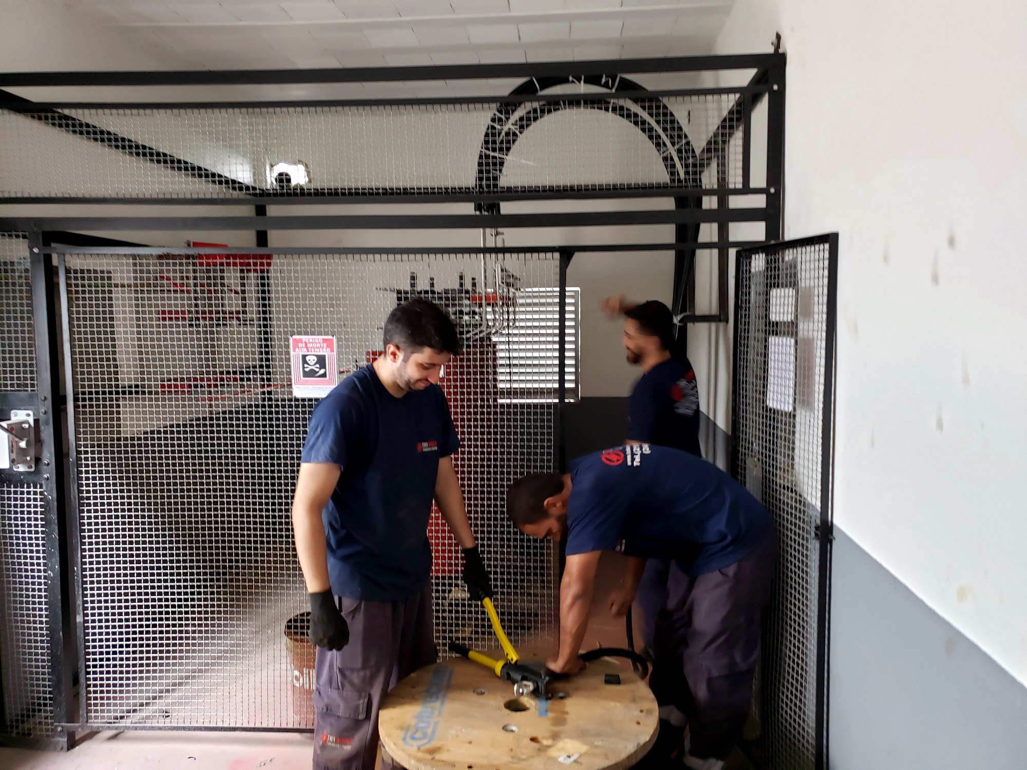 Técnicos crimpando terminais de cabo com prensa em subestação